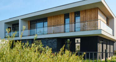 Side view of two storey cottage with group of windows and balcony on second floor situated in rural environment